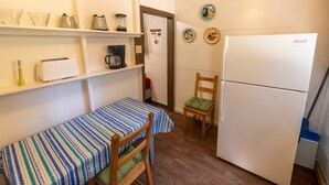 Ett kompakt kök med ett kylskåp, en kaffebryggare, en brödrost och ett litet matbord med ett randigt bordsduksöverdrag.