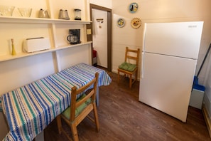 A compact kitchen with a refrigerator, a coffee maker, a toaster, and a small dining table with a striped tablecloth.