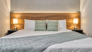Ein Hotelzimmer mit hölzernem Kopfteil, zwei Nachttischlampen, einem Bett mit gemustertem Überwurf und einer strukturierten Wand.