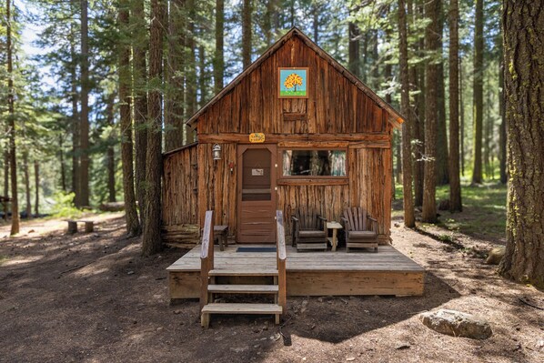 Una cabaña rústica con terraza de madera, una puerta y un ventanal.