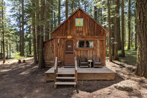 A rustic cabin with a wooden deck, a door, and a window.