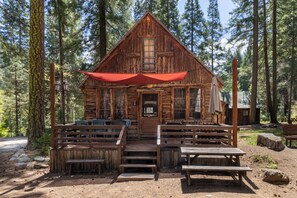 A rustic cabin with a porch, wooden benches, and a red awning.
