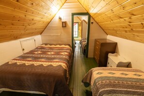 A narrow attic bedroom with two beds, a dresser, and a small window.