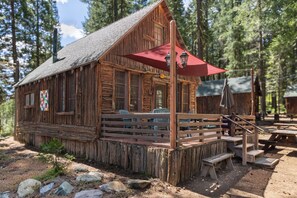 A rustic cabin with a wooden porch, a red awning, and a stone pathway leading to a wooden bench.