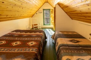 A small attic room with two beds, a chair, and a window with green shutters. - Two-Story Pine Cabin at Camp Layman | Spacious Mountain Lodge for Eight (Blairsden-Graeagle)