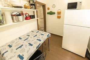 A kitchen with a table, a refrigerator, and various kitchen items on shelves.