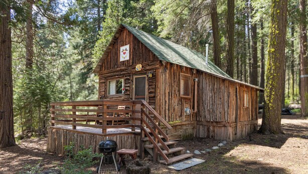A rustic cabin with a wooden deck, a chimney, and a sign indicating it's a campground.