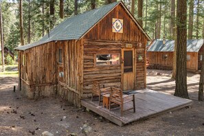 A rustic cabin with a wooden exterior, a porch with benches, and a small window. - Nimble Squirrel Cabin at Camp Layman | Playful Mountain Retreat with King Bed (Blairsden-Graeagle)