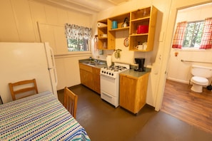 A compact kitchen with a stove, sink, and wooden cabinets. There is a dining table with a patterned tablecloth. - Accessible Cub Cabin at Camp Layman | Playful & Inclusive Riverside Stay (Blairsden-Graeagle)