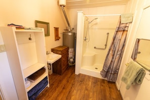 A bathroom with a sink, wooden cabinet, shower with curtain, and a towel rack. - Accessible Cub Cabin at Camp Layman | Playful & Inclusive Riverside Stay (Blairsden-Graeagle)