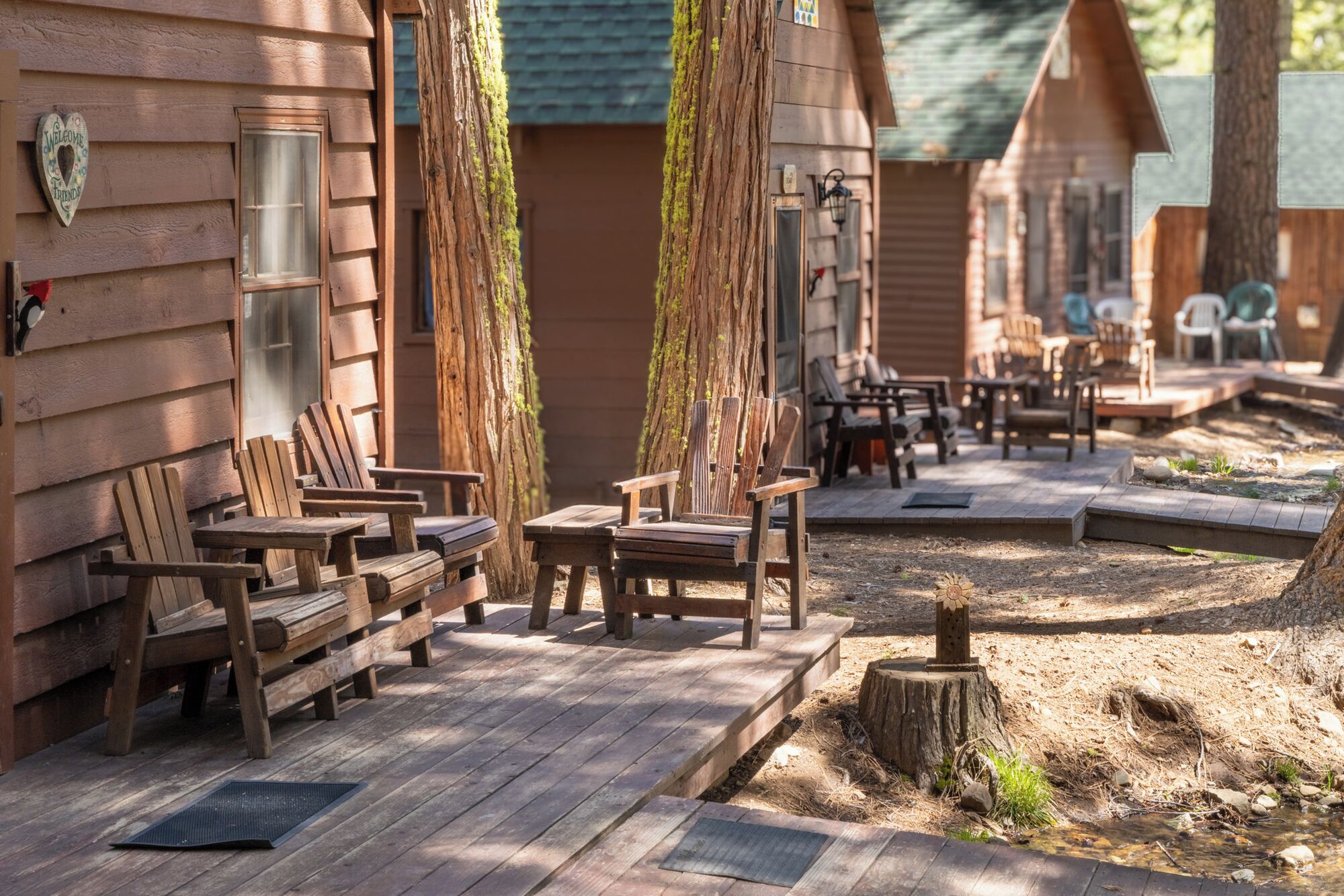 A row of wooden cabins with outdoor seating and a small stream.
