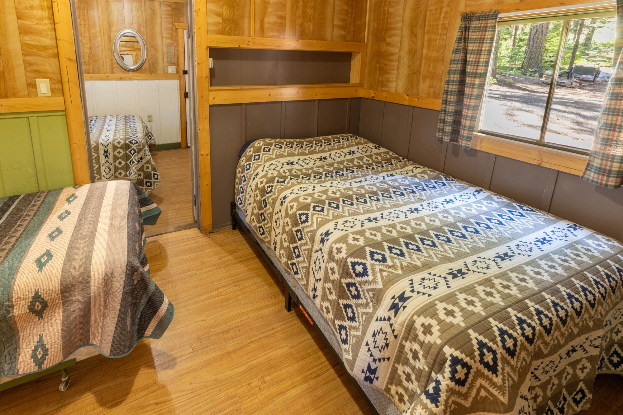 Een kamer met een bed, een bankje, een raam met uitzicht op bomen en een spiegel aan de muur.