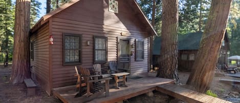 A cabin with a porch, wooden chairs, a table, and a small deck.