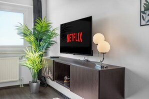 Ein modernes Wohnzimmer mit einem Flachbildfernseher, der an einer dunklen Holzkonsole befestigt ist, einer Topfpflanze und einer Wandleuchte.