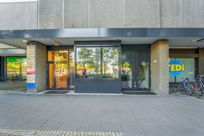 Ein Gebäudeeingang mit Glastür, Schild für einen Fahrradverleih und einem sichtbaren Fahrradstellplatz.