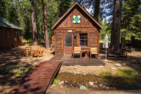 Une cabane rustique dotée d’une terrasse en bois, d’un petit porche et d’un panneau indiquant qu’il s’agit d’une zone de pêche à la truite.