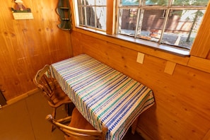 Een houten kamer met een tafel, stoelen, een raam en een wandlamp.