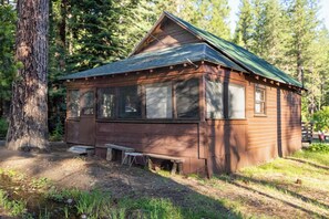 Une cabane rustique avec un toit végétalisé, de grandes fenêtres et un banc  à l’extérieur.