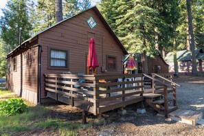 A wooden cabin with a porch, a red umbrella, and a small deck.