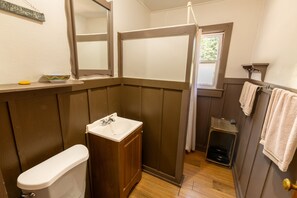 Une salle de bain avec un meuble-lavabo en bois, des toilettes, un lavabo, une fenêtre et un porte-serviettes.
