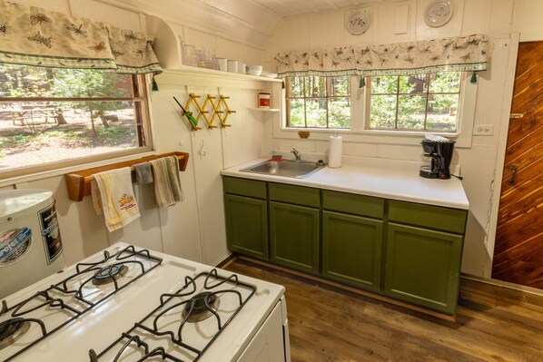A kitchen with a gas stove, a sink, green cabinets, and a window with a view of greenery.