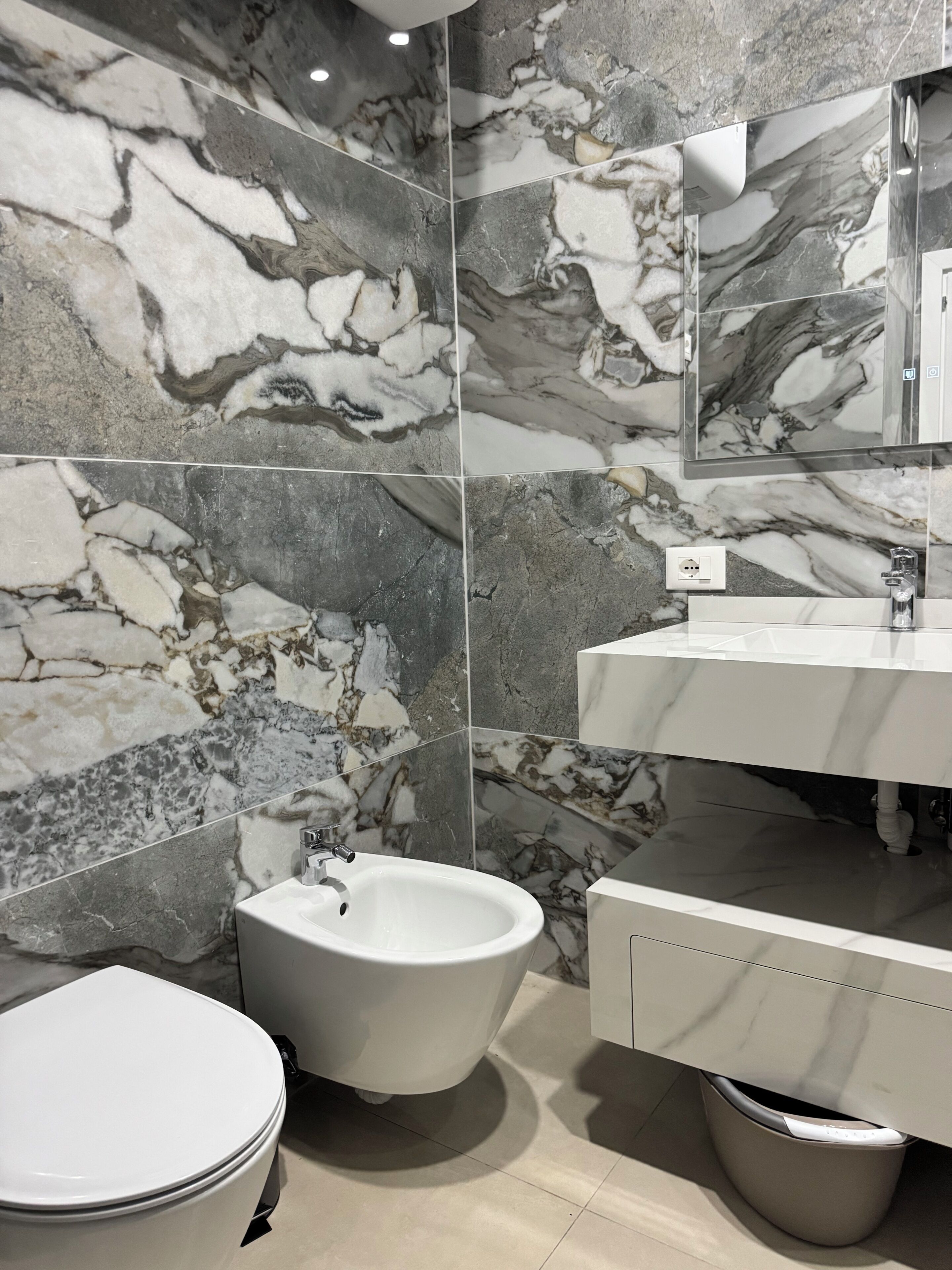 A bathroom with a bidet, a toilet, a sink, and a mirror.