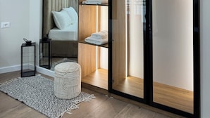 Habitación de hotel moderna con cama, armario con repisas iluminadas, una mesita con lámpara y un tapete decorativo.