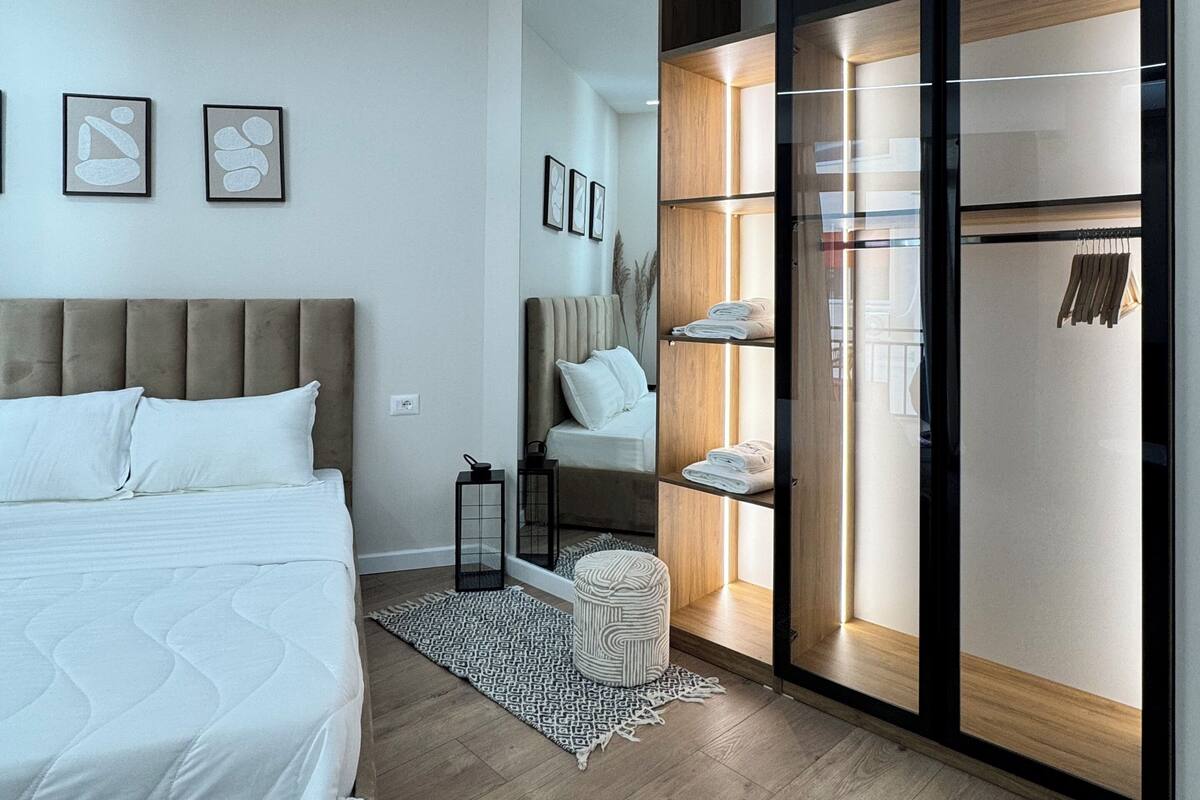 Un dormitorio moderno con cama, una silla, un armario y una mesita.