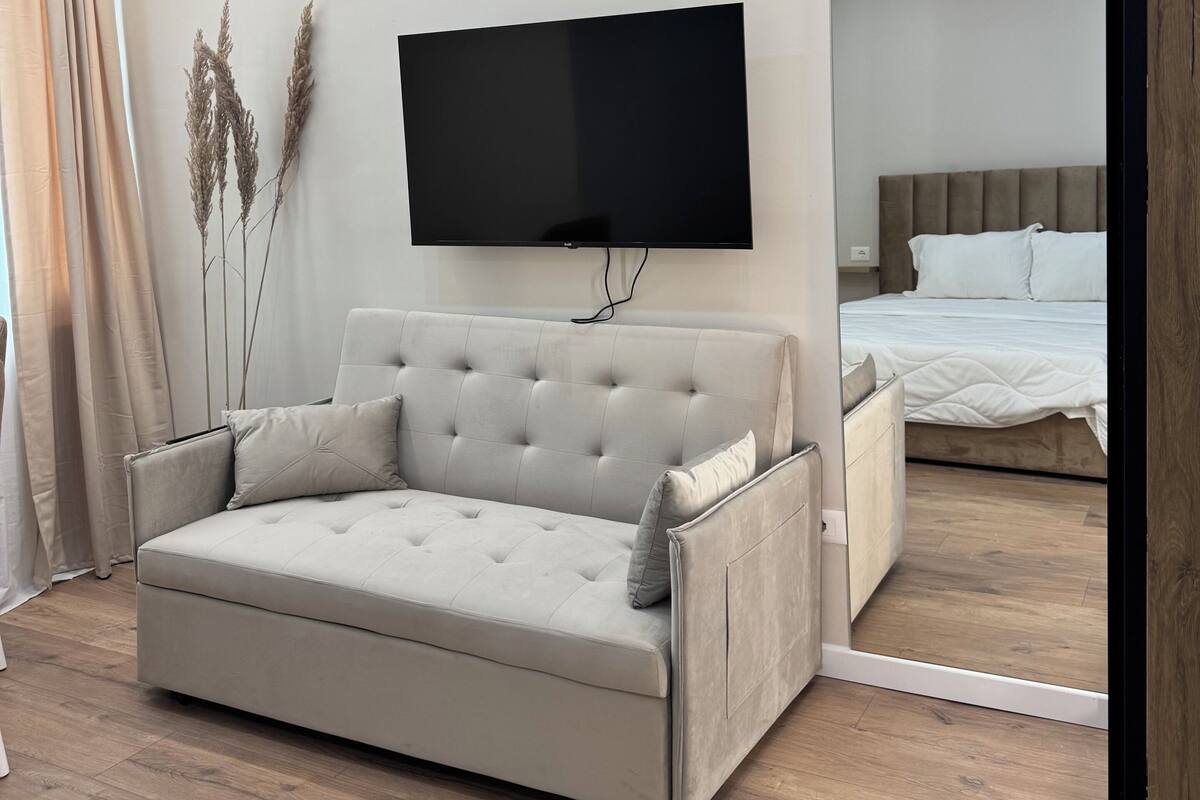 Un dormitorio moderno con sofá, cama, televisor de pantalla plana y piso de madera.