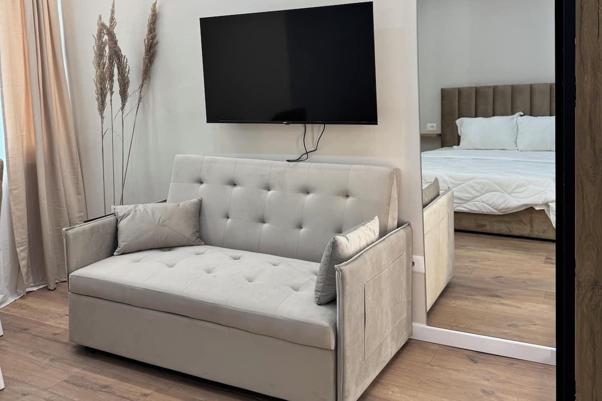 A modern bedroom with a sofa, a bed, a flat-screen TV, and a wooden floor.