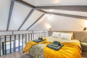 Ein Schlafzimmer mit schrägen Wänden, einem Bett mit gelber Decke und einem Balkon mit Geländer.