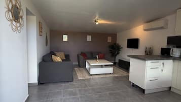 Una sala de estar moderna con un sofá gris, una mesa de centro blanca y una cocina con un armario blanco y microondas.