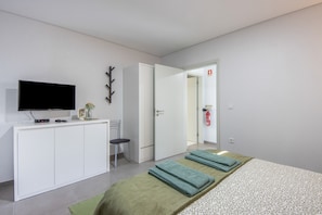Ein modernes Hotelzimmer mit Bett, Schreibtisch, Flachbildfernseher, Sessel und einer Tür zu einem weiteren Raum.
