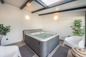 Ein Wellnessraum mit Whirlpool, zwei weißen Stühlen, einer Bambuspflanze und einem Oberlicht.