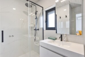 Ein modernes Badezimmer mit Duschkabine aus Glas, einem weißen Waschtisch mit Spiegel und einem Fenster über dem Waschbecken.