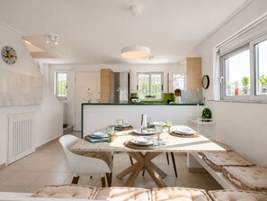 A modern kitchen with a dining area, a refrigerator, and a window with plants.