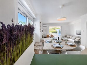 Un espace repas moderne avec une table dressée pour quatre personnes, un canapé et une vue sur l’extérieur.