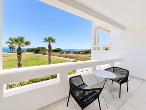 Un balcon avec vue sur la mer, deux chaises et une petite table.