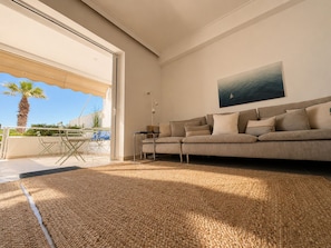 A modern living room with a sofa, a painting, and a view of the outdoors.