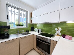 Moderni keittiö, jossa on ikkuna, ruostumattomasta teräksestä valmistetut kodinkoneet ja vihreät laatat seinässä.