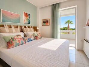 Une chambre à coucher avec un lit, des oreillers, une tête de lit, une fenêtre donnant sur un beau paysage et des œuvres d’art accrochées aux murs.