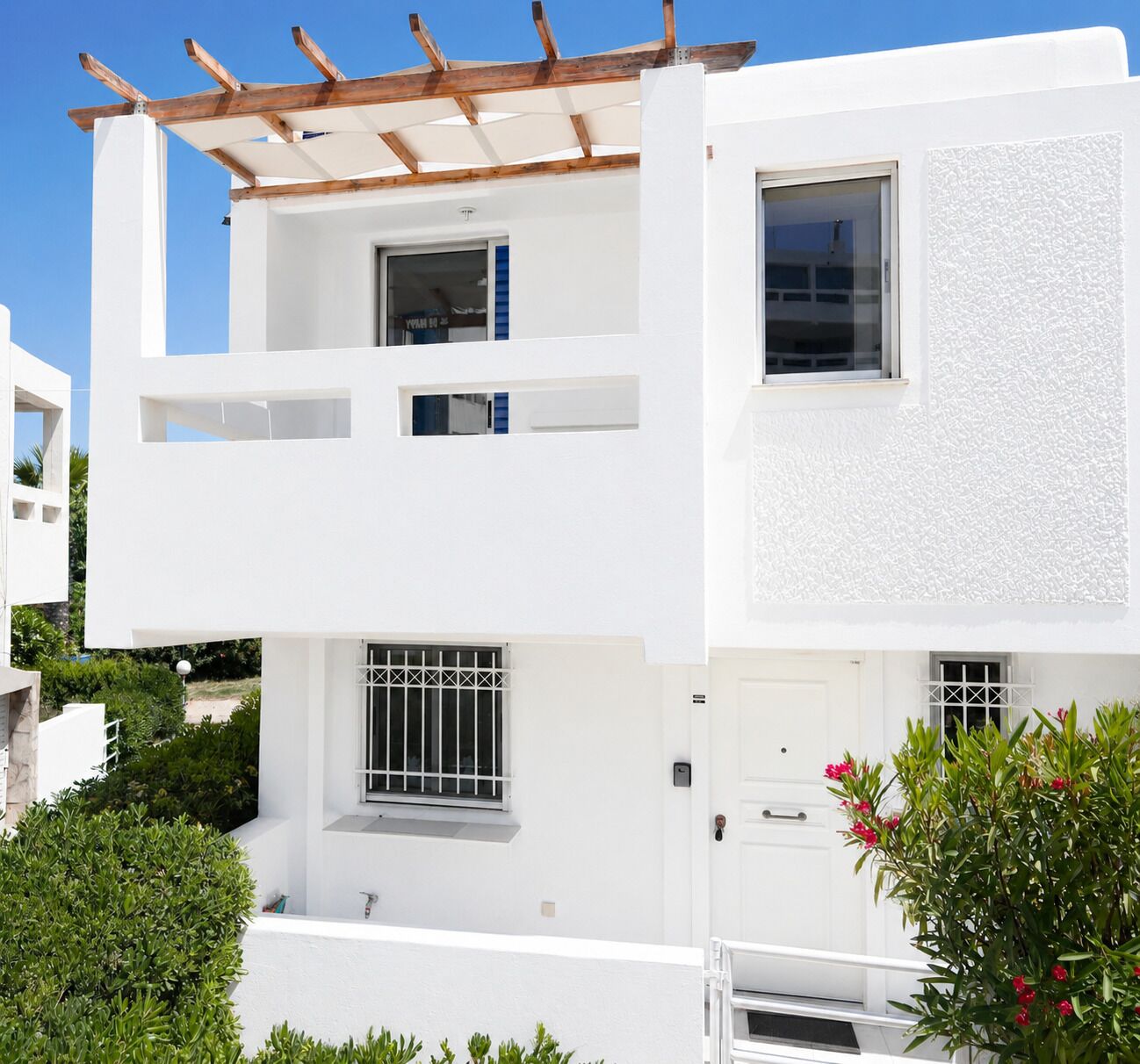 A modern two-story white building with balconies, a pergola, and a small garden area.