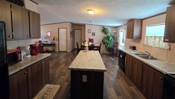 A kitchen with wooden cabinets, a central island, a dining area with chairs, a refrigerator, and a coffee maker. - 2-bedroom mobile home a minute off the Suncoast Parkway. Comfy and cozy! (Homosassa)
