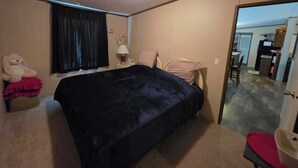 A bedroom with a bed, a nightstand, a lamp, a teddy bear, and a window with curtains. - 2-bedroom mobile home a minute off the Suncoast Parkway. Comfy and cozy! (Homosassa)