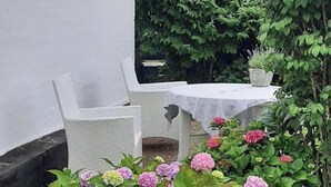 En terrasse med fletningsmøbler, et bord dækket med dug, og hortensia buske.