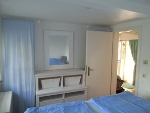 Ein Schlafzimmer mit einem Bett, einem Kleiderschrank, einem Spiegel und einer Tür zu einem anderen Raum.