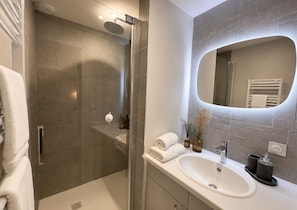 Une salle de bain moderne avec une douche à parois de verre, un lavabo blanc, un grand miroir et un porte-serviettes.