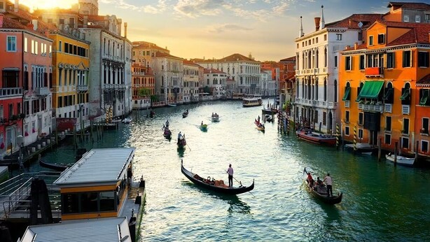 Un canal con góndolas, edificios históricos y un puente.