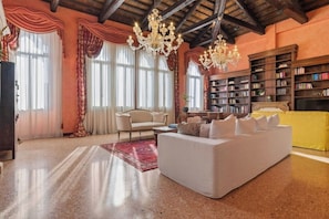 Un salon spacieux avec un grand canapé blanc, une bibliothèque et un lustre.