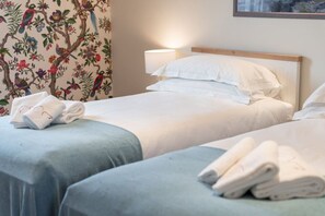 Une chambre d’hôtel avec deux lits, une table de chevet avec une lampe et un papier peint à motifs floraux.